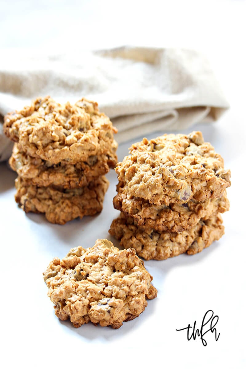 Vertical image of stacks of Gluten-Free Vegan Peanut Butter Chocolate Chip Oatmeal Cookies on a white surface next to a cream cloth napkin