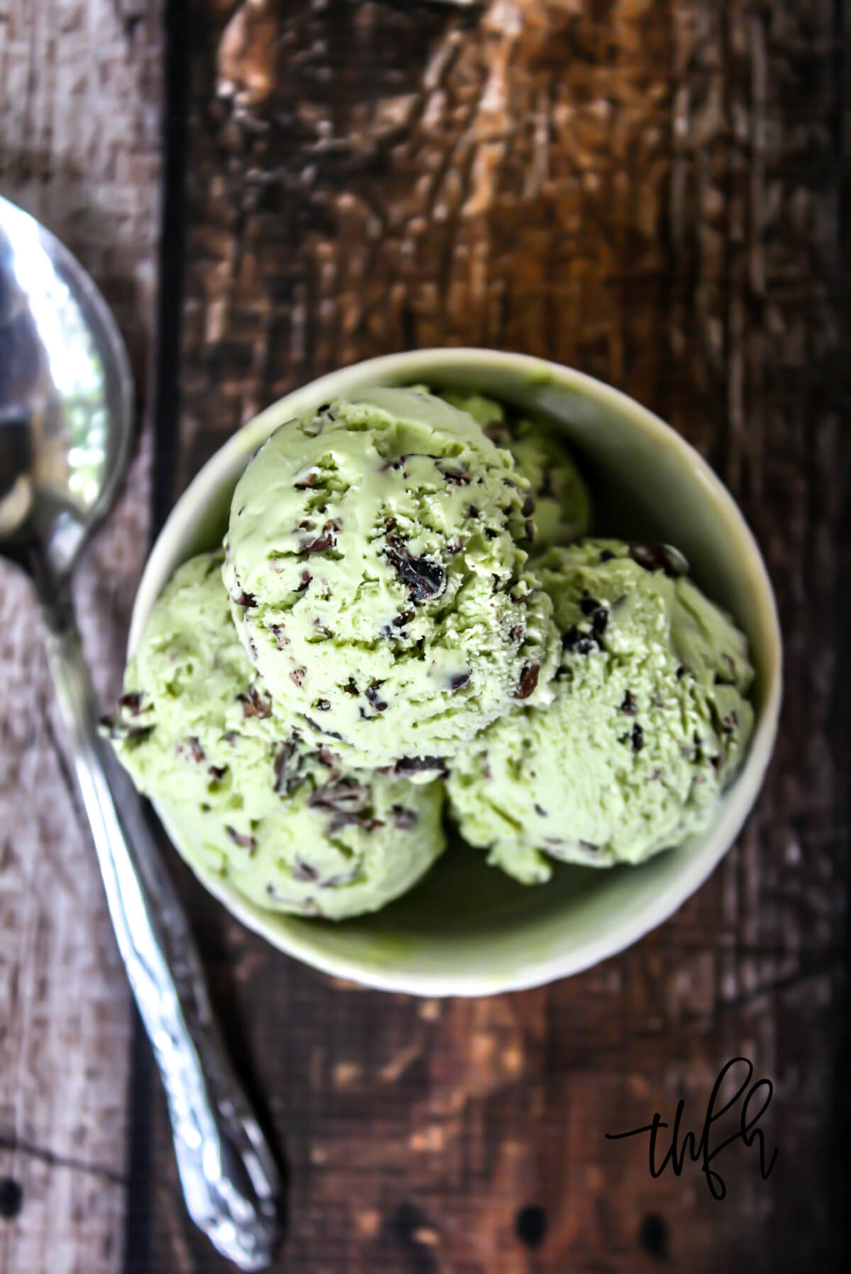 Overhead vertical image of a small bowl filled with light green ice cream on a weathered wooden surface