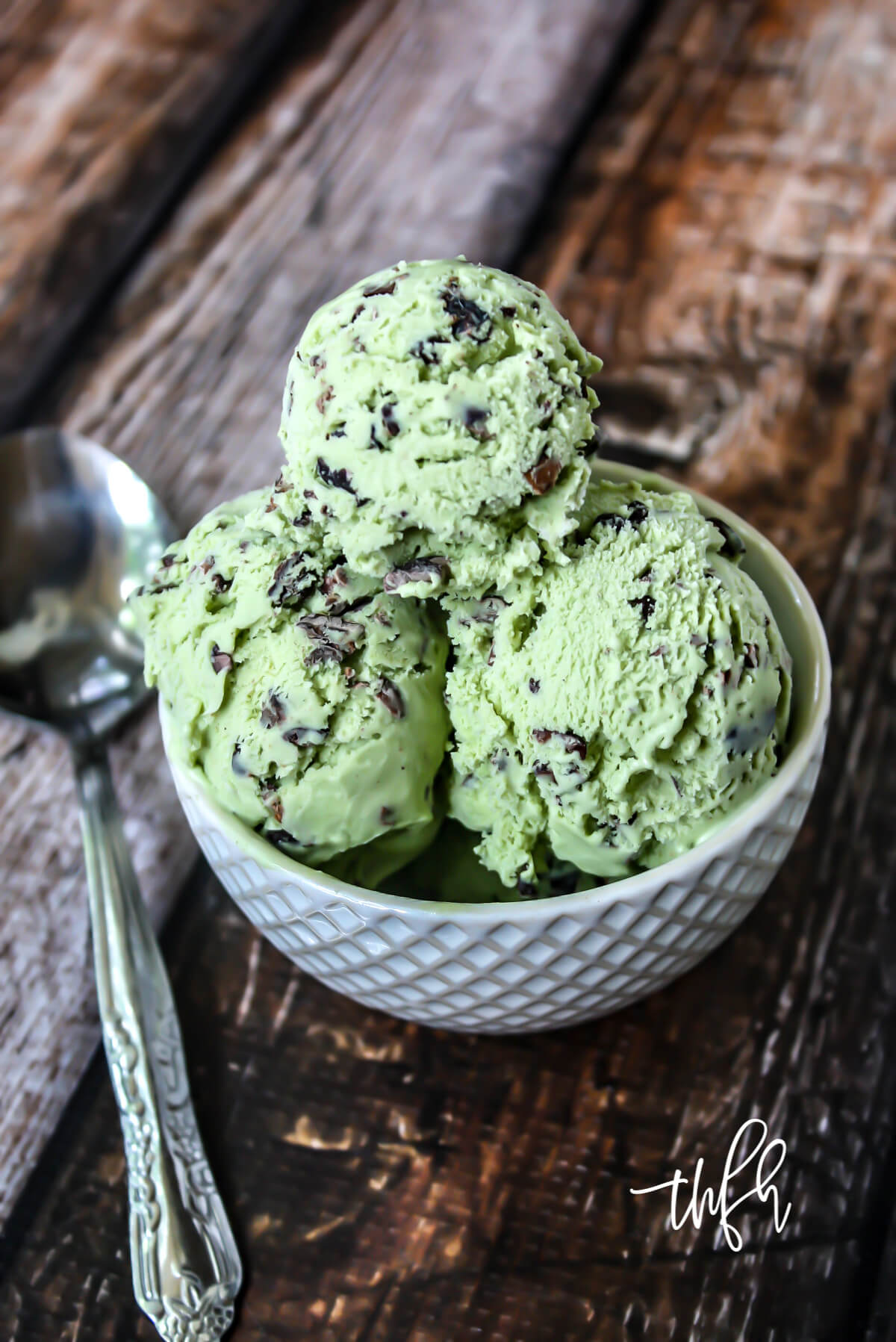 Vertical image of light green ice cream in a small decorative white bowl on a weathered wooden surface