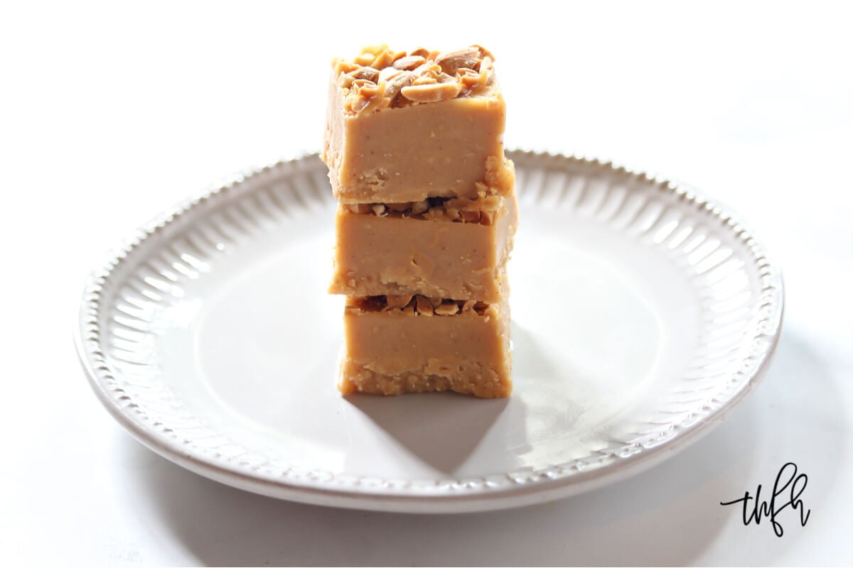 A stack of three squares of peanut butter fudge on a grey decorative plate on a white background