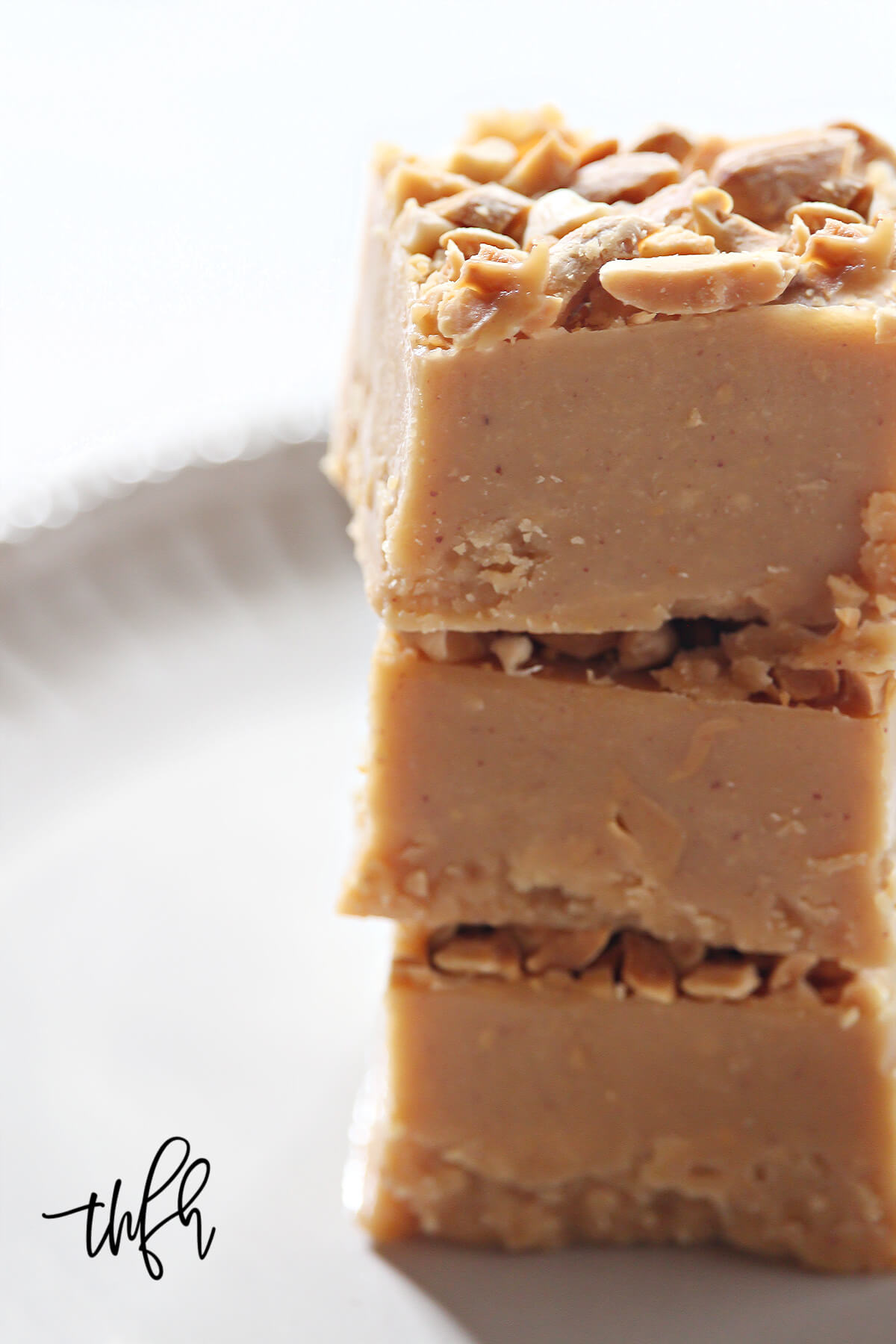 Close up image of a stack of three squares of peanut butter fudge on a decorative grey plate on a white background