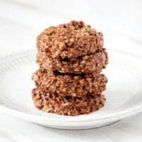Horizontal image of a stack of 4 Healthy Gluten-Free Vegan Chocolate Peanut Butter Oatmeal No-Bake Cookies on a white plate on top of a white marble surface