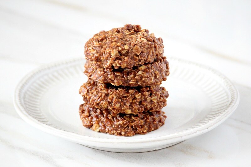 Horizontal image of four of The ORIGINAL Healthy Gluten-Free Vegan No-Bake Chocolate Peanut Butter Oat Cookies stacked on a white plate on a white marble background