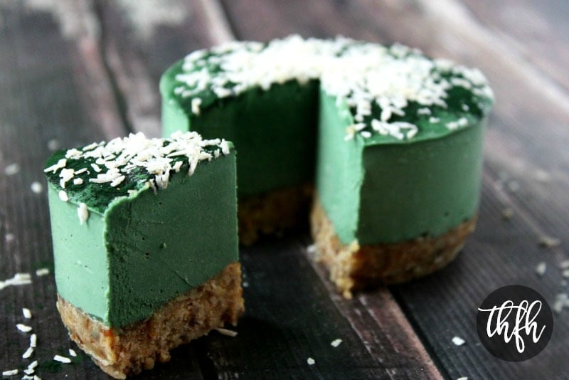 A 6-inch Gluten-Free Vegan Raw No-Bake Spirulina Cheesecake with a large slice cut out in the foreground showing the inside of the cheesecake placed on a weathered wooden surface 