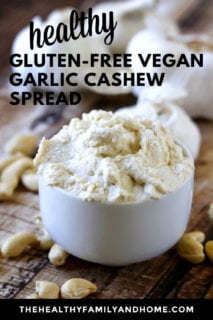 Vertical image of a small dip bowl filled with Gluten-Free Vegan Garlic Cashew Spread on a weathered wooden surface with text overlay