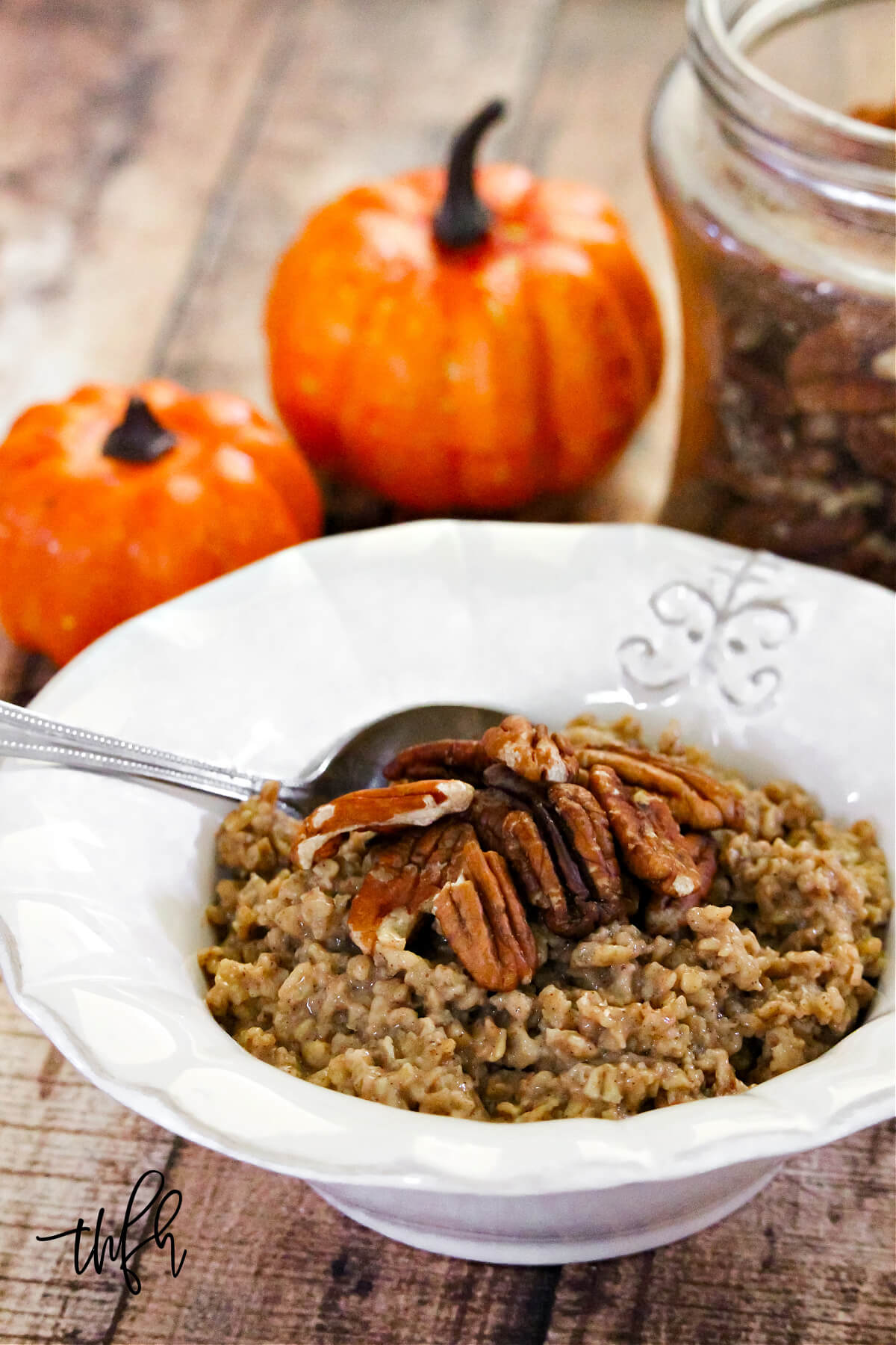 Vertical image of a white bowl of oatmeal next to two small pumpkins on a weathered wood surface