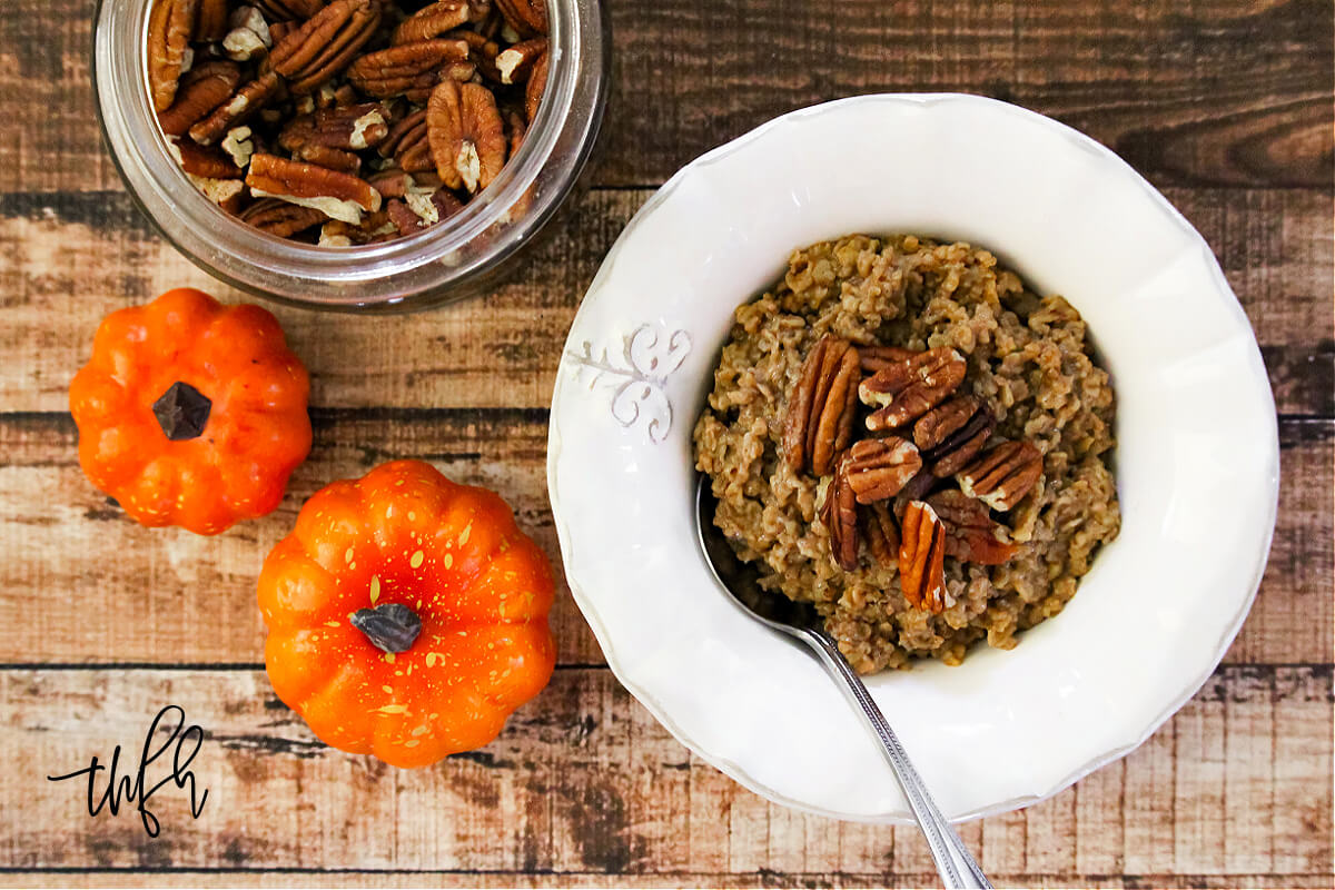 Overhead image of a white bowl of oatmeal next to two small pumpkins on a weathered wood surface