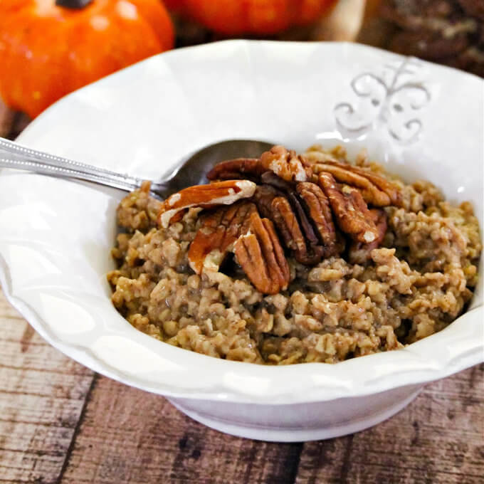 Close up image of a white bowl of oatmeal next to two small pumpkins on a weathered wood surface