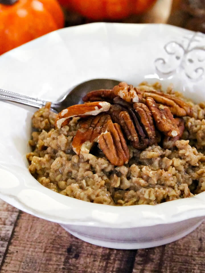 Close up image of a white bowl of oatmeal next to two small pumpkins on a weathered wood surface
