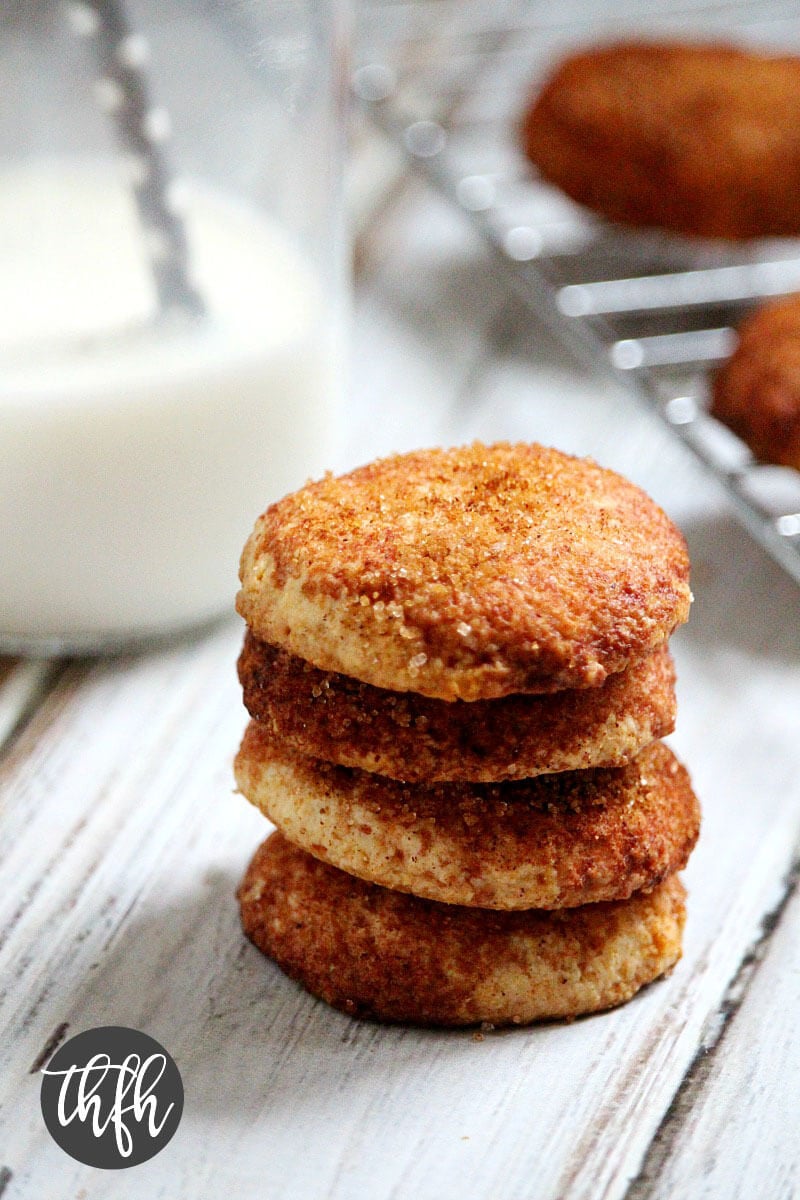 Stack of 4 Gluten-Free Vegan Flourless Snickerdoodle Cookies on a white wooden surface with a glass of milk in the background