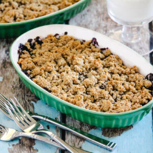 Green oven baking dish filled with blueberry cobbler on a weathered wooden surface