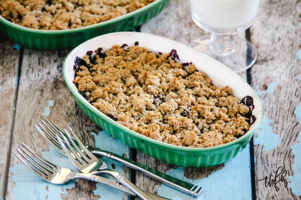 Green oven baking dish filled with blueberry cobbler on a weathered wooden surface