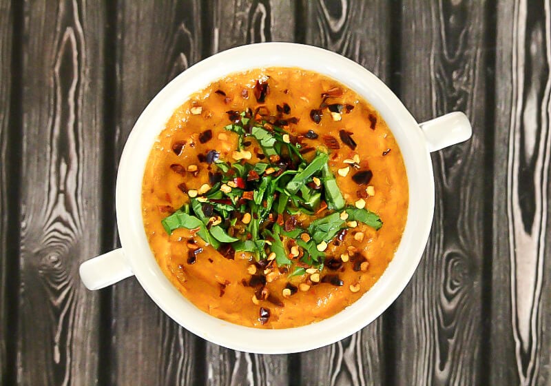 Overhead image of a grey bowl filled with Gluten-Free Vegan Spicy Roasted Red Pepper and Garlic Soup garnished with chopped spinach and red pepper flakes 