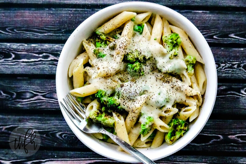 Overhead view of Gluten-Free Vegan Broccoli Alfredo with Creamy Cauliflower Sauce in a white bowl on a black wooden surface