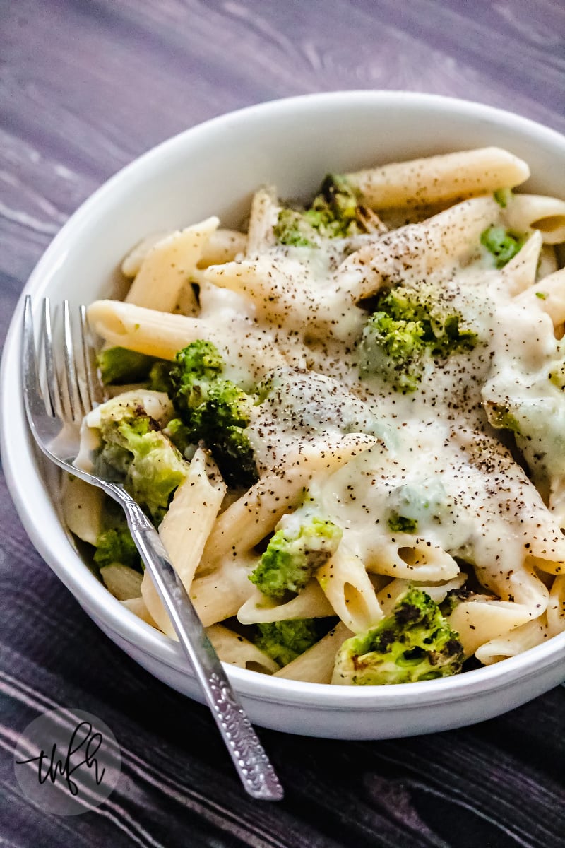 Vertical image of Gluten-Free Vegan Broccoli Alfredo with Creamy Cauliflower Sauce in a white bowl on a black wooden surface
