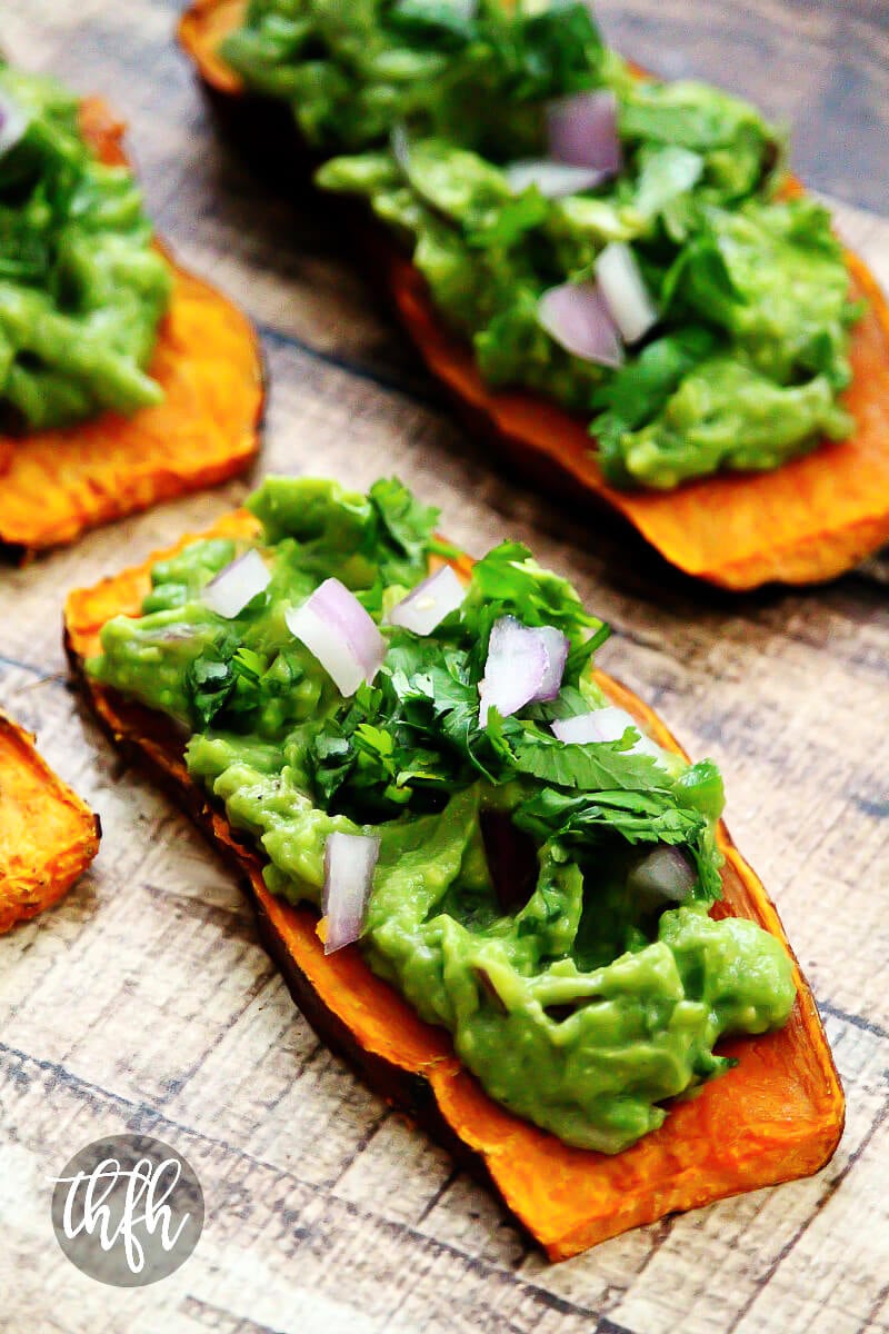 Close-up image of a slice of sweet potato "toast" topped with spicy guacamole on a weathered wooden surface