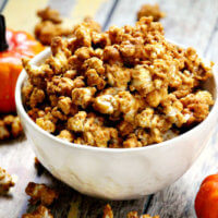 Horizontal image of a white bowl filled with The BEST Gluten-Free Vegan Pumpkin Spice Caramel Popcorn on a wooden surface