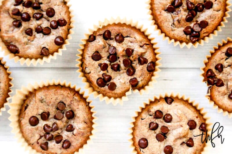 Overhead image of multiple chocolate chip pumpkin muffins in brown paper muffin cups on a white wooden surface