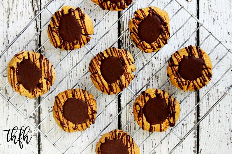 Overhead view of Gluten-Free Vegan Flourless Chocolate Peanut Butter Thumbprint Cookies on a wire cookie rack on top of a white wooden surface.