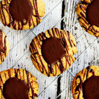 Overhead view of Gluten-Free Vegan Flourless Chocolate Peanut Butter Thumbprint Cookies on a wire cookie rack on top of a white wooden surface
