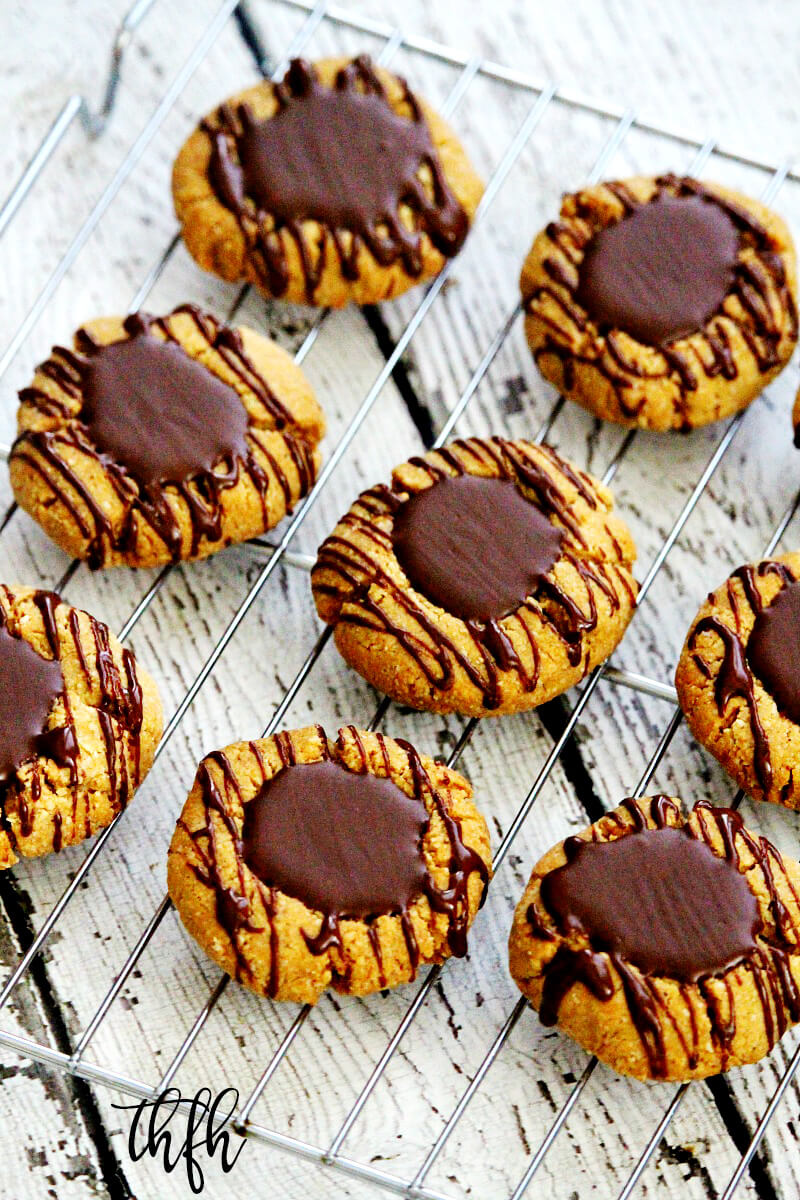 Angled overhead shot of Gluten-Free Vegan Flourless Chocolate Peanut Butter Thumbprint Cookies on a wire cookie rack on top of a white wooden surface