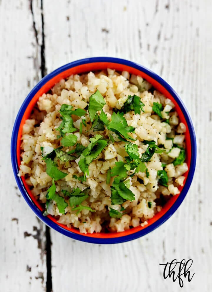 Vertical overhead view of Lectin-Free Vegan Cilantro and Lime Cauliflower Rice in a blue rimmed bowl on a white wooden surface