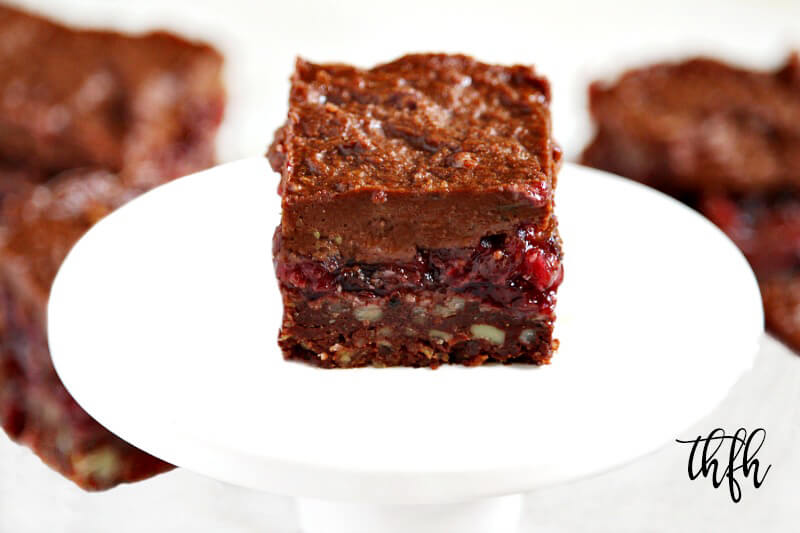 A square of gluten-free vegan raw no-bake black forest squares on a small white pedestal with more squares in the background.