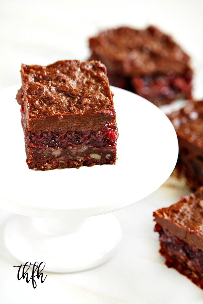 A vertical image of a white cake platter with a single Gluten-Free Vegan No-Bake Black Forest Bar in the center with three more bars to the right of it