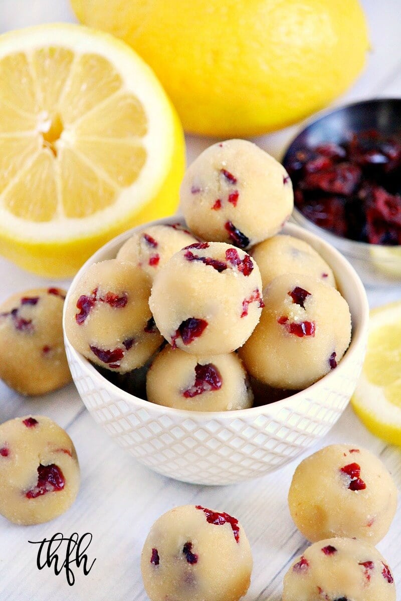 Vertical image of Gluten-Free Vegan No-Bake Cranberry Lemon Ball Truffles in a cream colored bowl surrounded by lemons and cranberries