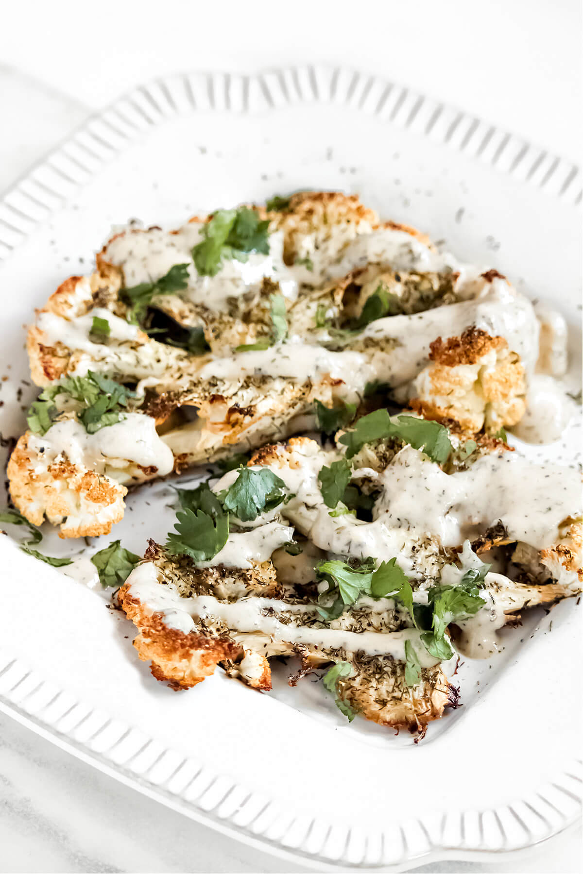 Close up of two cauliflower steaks drizzled with sauce on a decorative white plate