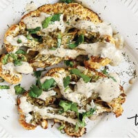 Horizontal image of Gluten-Free Vegan Roasted Cauliflower "Steaks" on a white plate on a white marble background
