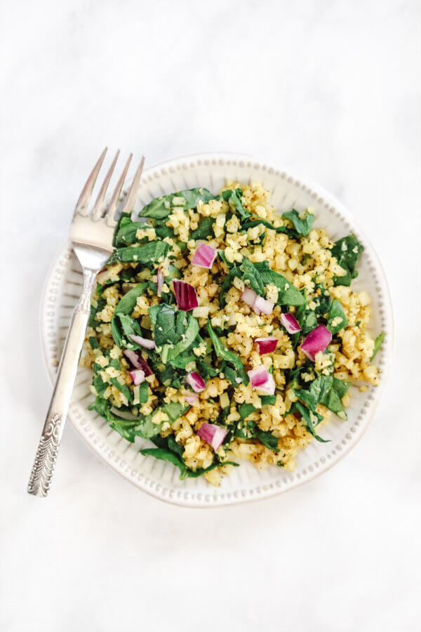 Overhead vertical image of Gluten-Free Vegan Black Pepper and Turmeric Cauliflower Rice on a white plate with fork on a white marble surface