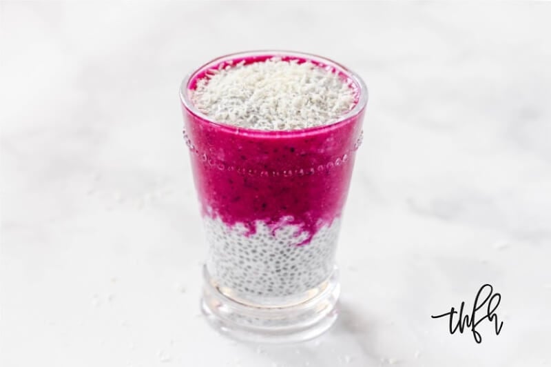 Horizontal image of Gluten-Free Vegan Pitaya Dragon Fruit Chia Seed Pudding in a glass on a white marble surface