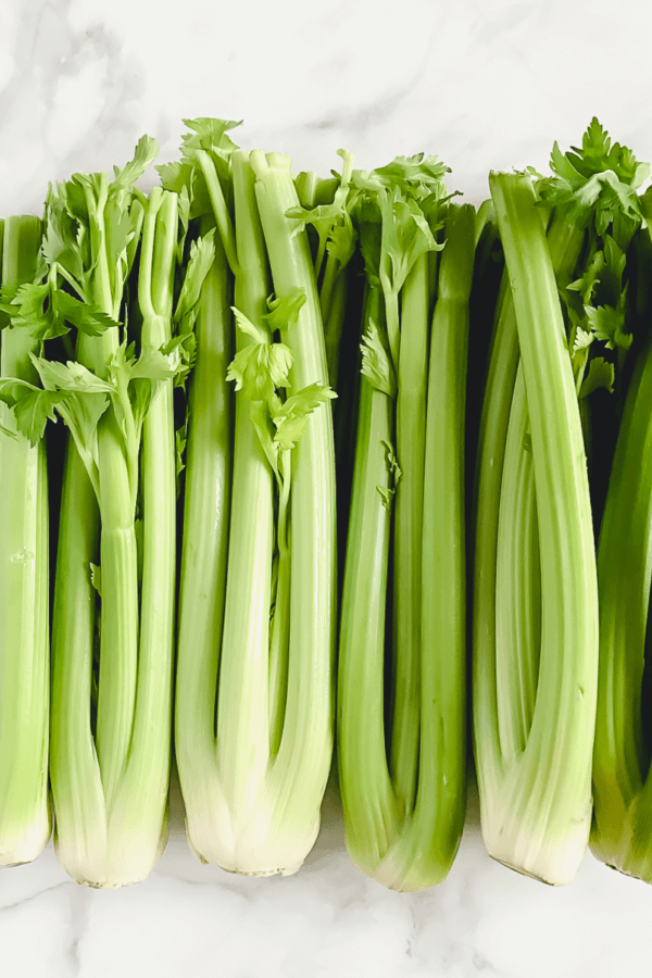 Vertical image of organic raw celery on a white marble surface