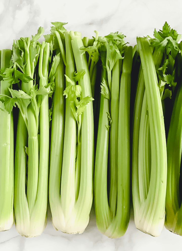 Vertical image of organic raw celery on a white marble surface