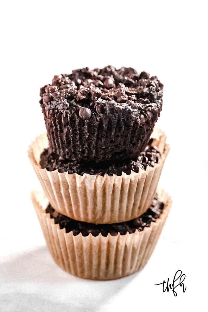 Vertical image of a stack of 3 Gluten-Free Vegan Flourless Chocolate Zucchini Muffins in paper muffin cups on a white background