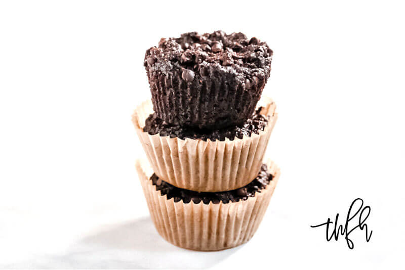 Horizontal view of a stack of 3 Gluten-Free Vegan Flourless Chocolate Zucchini Muffins in paper muffin cups on a white background