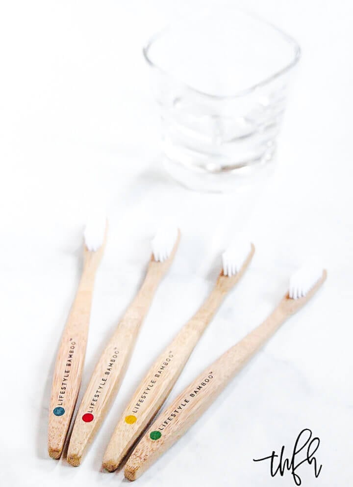 Four LIFESTYLE BAMBOO Eco-Friendly Toothbrushes on a white marble surface with a glass in the background