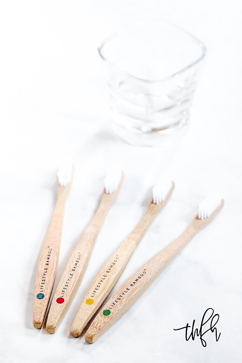 Four LIFESTYLE BAMBOO Eco-Friendly Bamboo Toothbrushes on a white marble surface with a glass in the background