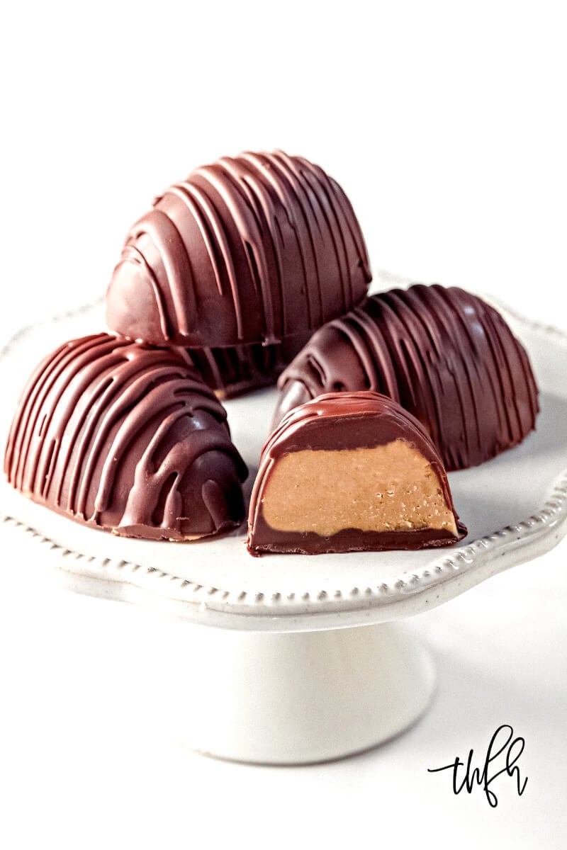 Vertical image of 4 Gluten-Free Vegan Healthy Reese's Peanut Butter Eggs on a small white pedestal on a white background