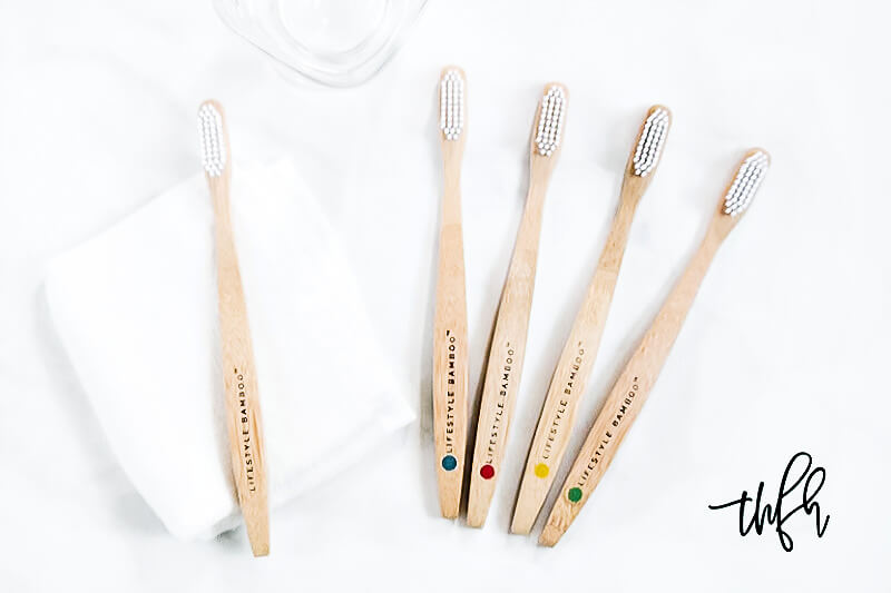 Collection of 5 LIFESTYLE BAMBOO Eco-Friendly Bamboo Toothbrushes on a white marble surface and white washcloth with glass in background