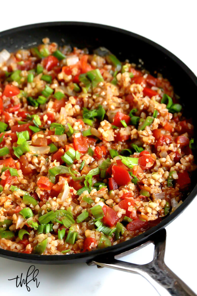 Overhead vertical angled view of Gluten-Free Vegan Spicy Mexican "Spanish" Cauliflower Rice recipe in a black skillet on a white marbled surface