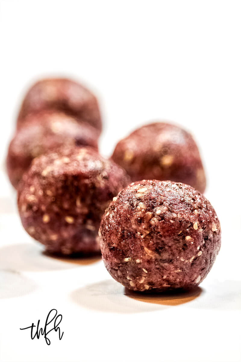 Vertical View of five Gluten-Free Vegan Healthy Triple Seed Energy Balls on a solid white surface