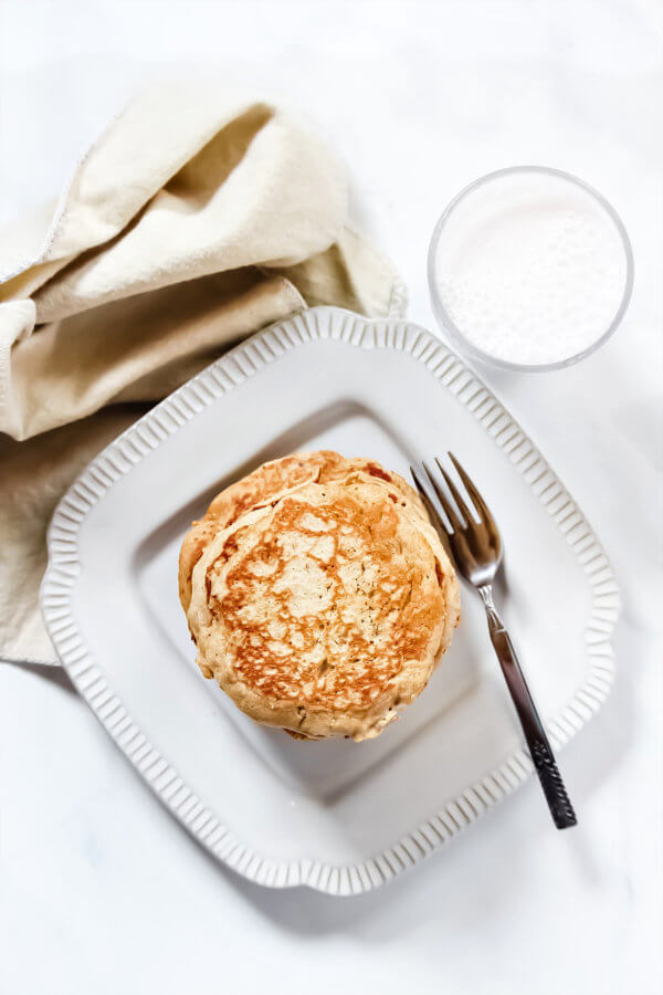 Overhead image of a decorative grey plate with a stack of Gluten-Free Vegan Pumpkin Spice Blender Pancakes on it with a glass of milk and cream cloth napkin to the side of the plate