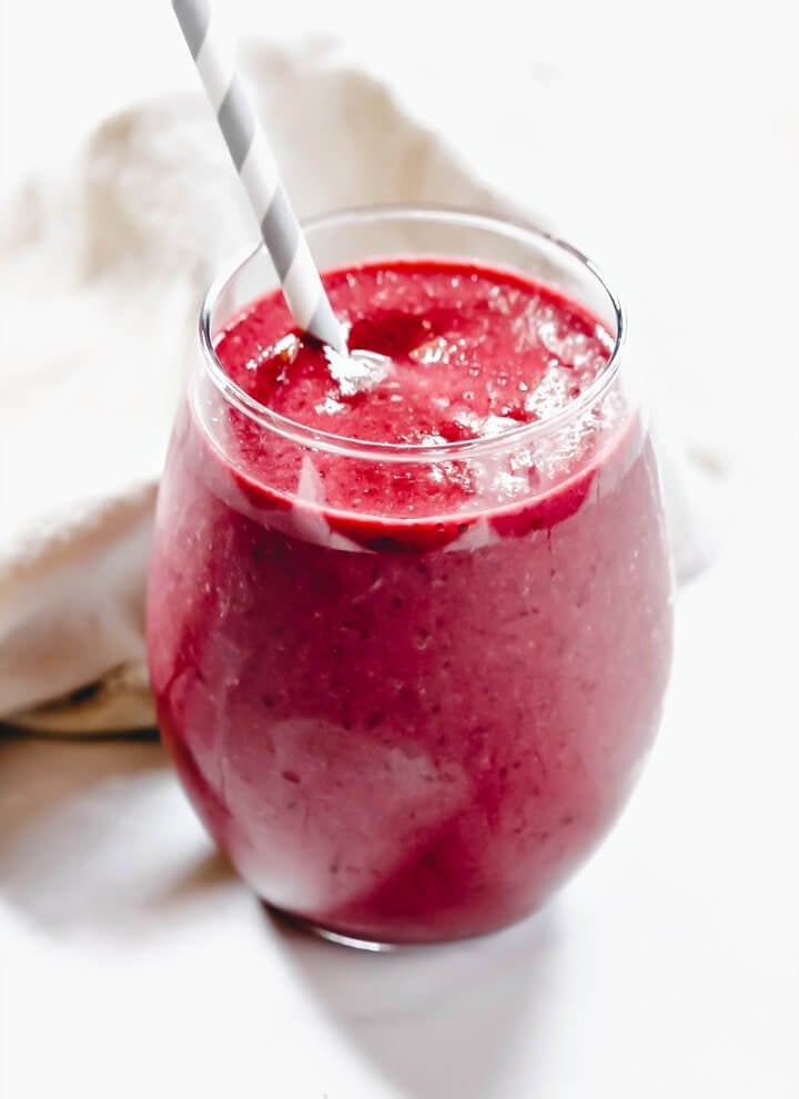 Close up image of a glass filled with The BEST Vegan Cherry and Banana Smoothie with a grey and white straw inserted in the glass