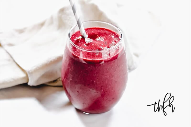 Horizontal image of a glass of The BEST Vegan Cherry Banana Smoothie on a solid white surface 