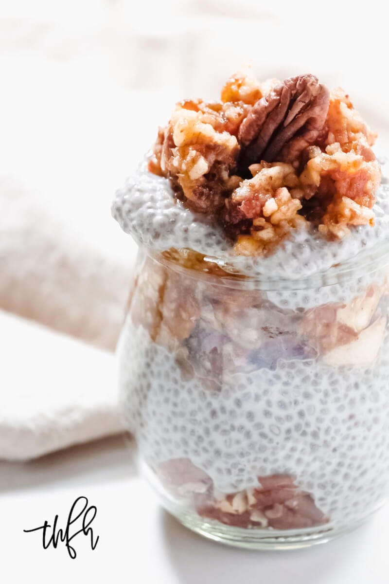 Close-up vertical image of a glass filled with Gluten-Free Vegan Apple Pie Chia Seed Pudding with multiple layers and garnished with a large pecan