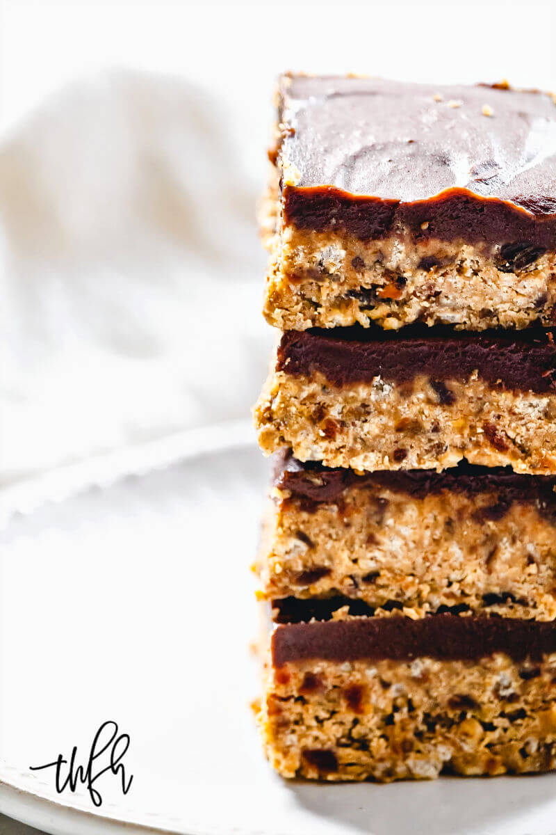 Close-up image of four squares of Gluten-Free Vegan No-Bake Crispy Pumpkin Spice Squares with chocolate topping stacked on top of each other on a white plate