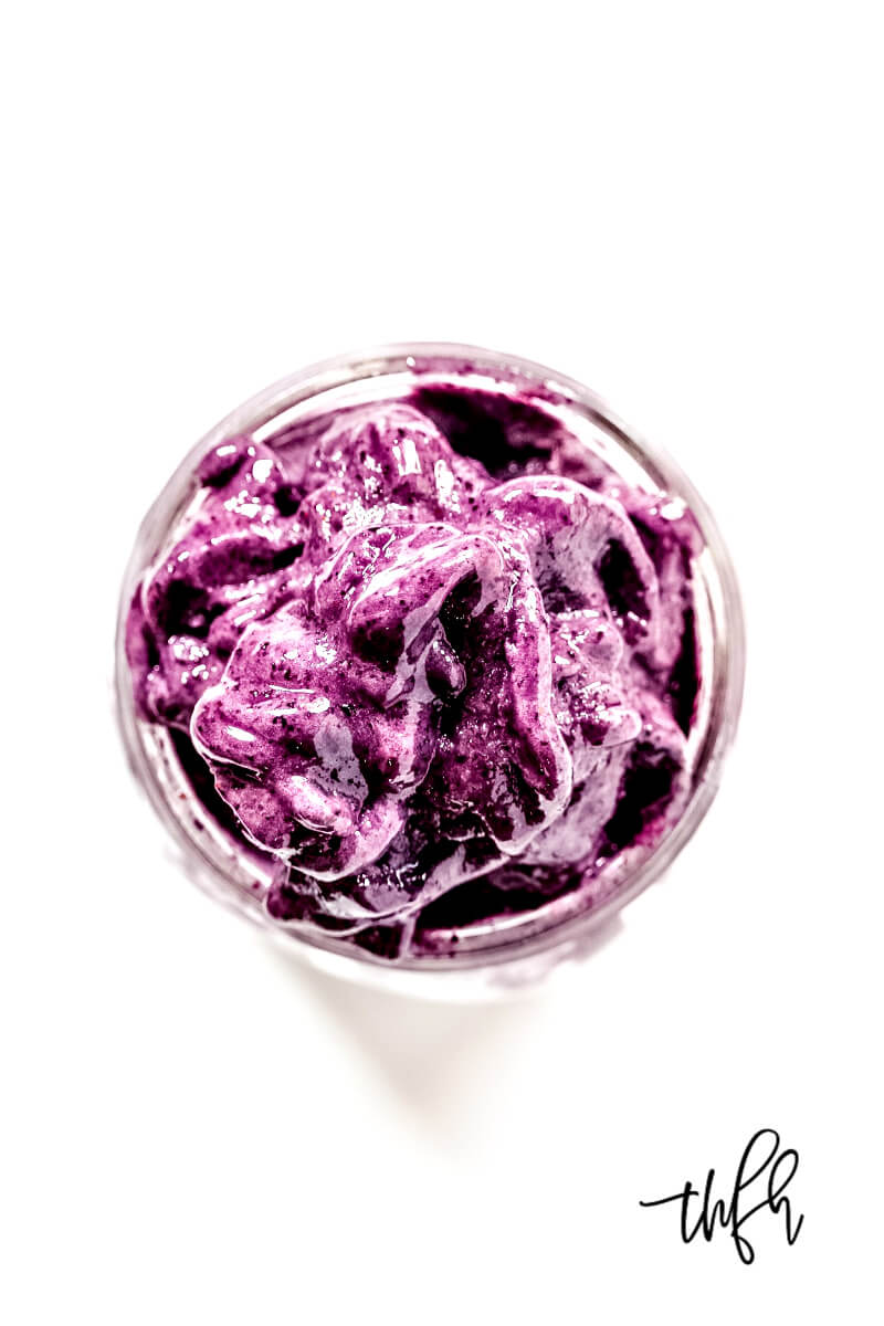 Overhead image of a thick purple smoothie in a glass on a solid white background