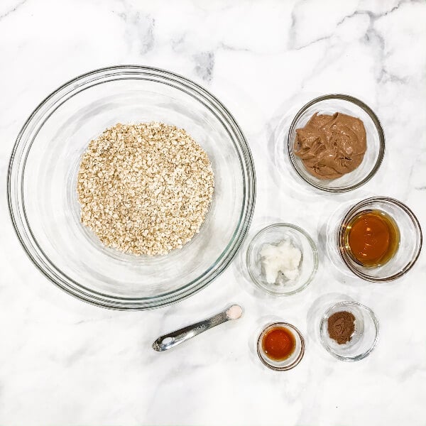 Image of all the ingredients needed to make Gluten-Free Vegan No-Bake Pumpkin Spice Granola Bars in individual glass bowls on a white marbled surface